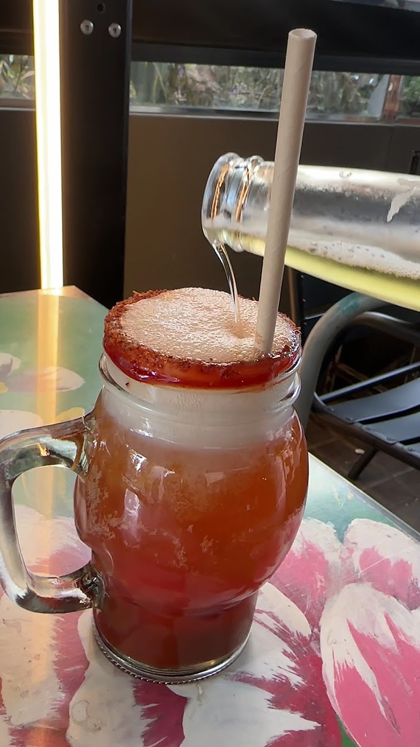 Cóctel de michelada en jarro con asa, borde de tajín y pajita